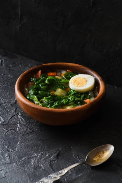 Edible wild herbs concept. Homemade rustic style soup with nettle and egg in wooden bowl with vintage fork on black background angle view copy space — Stock Image Edible Wild Herbs Concept Homemade Rustic Style Soup Nettle Egg Stock Photo
