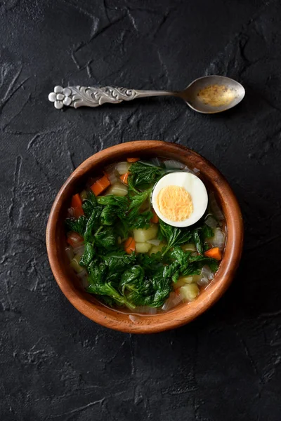 Wild herbs cooking. Rustic style vegetable soup with stinging nettle and boiled egg in wooden bowl with vintage spoon on black background top view copy space — Stock Image Wild Herbs Cooking Rustic Style Vegetable Soup Stinging Nettle Boiled Royalty Free Stock Images