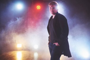 Stüdyoda mavi ışıklı, resmi kıyafetli yakışıklı bir adam var..