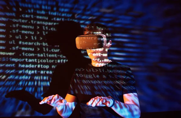 Double exposure of a caucasian man and Virtual reality VR headset is presumably a gamer or a hacker cracking the code into a secure network or server, with lines of code