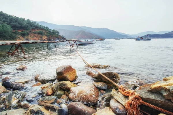 Kırık rıhtımın yakınındaki tekneler sakin, mavi bir deniz suyu koyuyor..