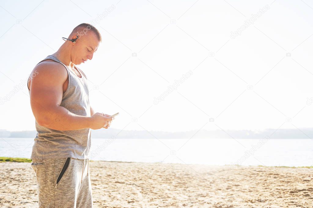A athletic man looking at the seaside on the wild sand beach. Masculine and sporty male with naked torso is doing evening training at the sea cost. Summer work-out training outdoors.