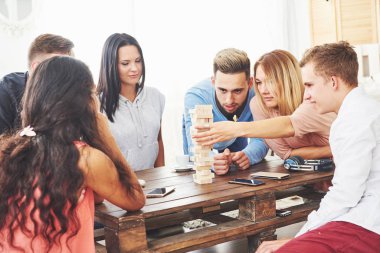 Bir grup yaratıcı arkadaş ahşap masada oturuyor. İnsanlar masa oyunu oynarken eğleniyor.