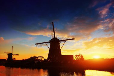 Rotterdam 'da deniz kenarındaki güzel geleneksel Hollanda değirmenleriyle muhteşem bir gün batımı ve suda yansıması olan bir manzara. Hollanda.