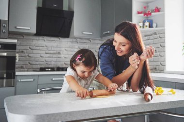 Mutfakta mutlu bir aile. Tatil yemeği konsepti. Anne ve kızı hamuru hazırlıyor, kurabiye pişiriyor. Evde kurabiye yapan mutlu bir aile. Ev yapımı yemek ve küçük bir yardımcı..