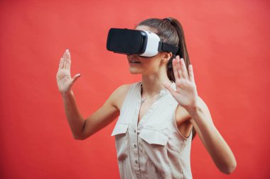 Stüdyoda kırmızı arka planda VR cihazı olan genç bir kadın..