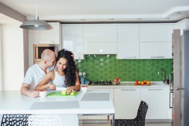 Güzel genç çift konuşuyor, kameraya bakıyor ve evde yemek pişirirken gülümsüyor..