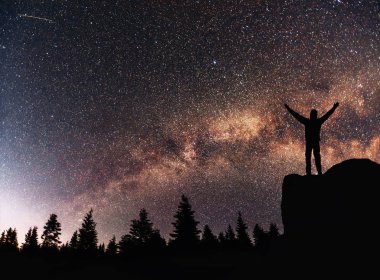 Saman Yolu 'nun arka planındaki siluet genç adam parlak bir yıldız olan karanlık gökyüzü tonunda..