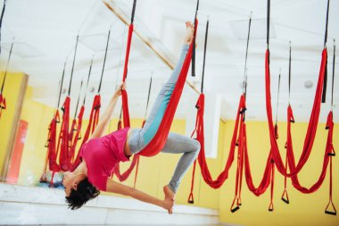 Genç ve güzel bir kadın parlak stüdyoda hamakla yoga yapıyor. Zihinsel ve fiziksel sağlık ve uyum kavramı