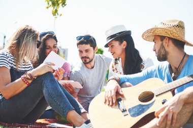 Mutlu genç arkadaşlarım parkta piknik. Onlar tüm mutlu, eğleniyor, gülümseyen ve gitar çalmak vardır.