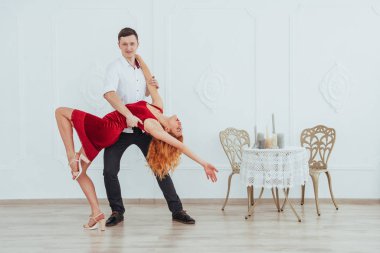 Kırmızı elbiseli genç bir kadın ve dans eden bir adam, stüdyoda beyaz bir arka planda izole edilmiş.