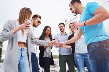 İskelenin kenarında oturan bir grup gencin portresi, doğada. Arkadaşlar gölde oyun oynuyorlar.