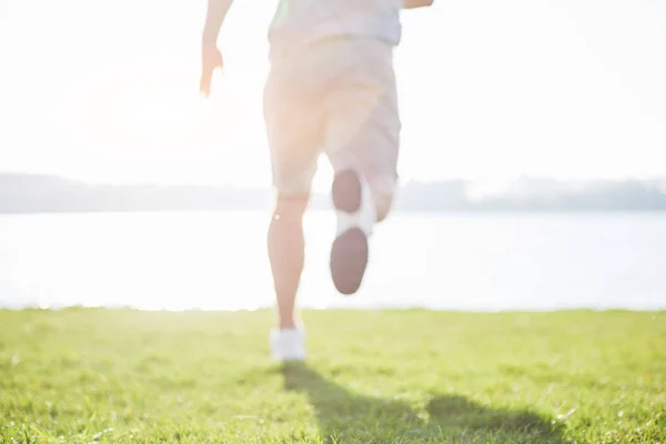 Outdoor cross-country running in summer sunshine concept for exercising, fitness and healthy lifestyle. Close up of feet of a man running in grass.