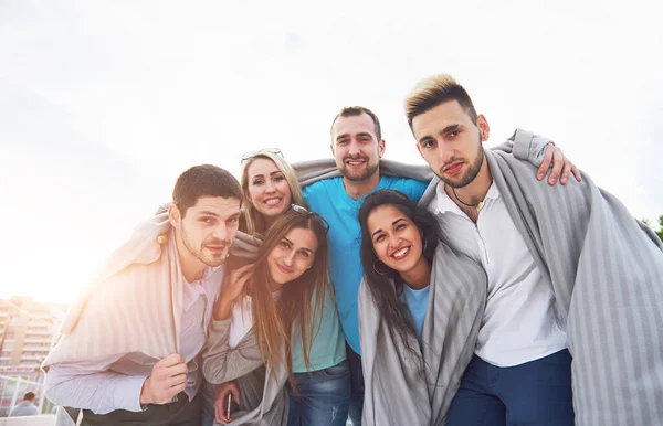 Portrait of a group of young people sitting on the edge of the pier, outdoors in nature. Friends enjoying a game on the lake. — Stock Photo, Image