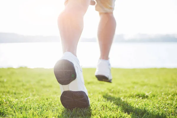 Outdoor cross-country running in summer sunshine concept for exercising, fitness and healthy lifestyle. Close up of feet of a man running in grass.