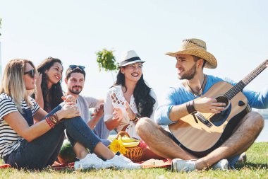 Mutlu genç arkadaşlarım parkta piknik. Onlar tüm mutlu, eğleniyor, gülümseyen ve gitar çalmak vardır.