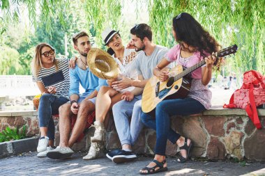 Gitarlı mutlu arkadaşlar grubu. Bir tanesi gitar çalarken diğerleri de onu alkışlıyor..