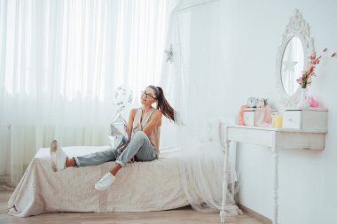 Stüdyodaki sevimli esmer kız, geniş bir gülümsemeyle şeffaf ve gümüş balonlarla oynuyor. Gözlük takıyor ve saçları kıvırcık..