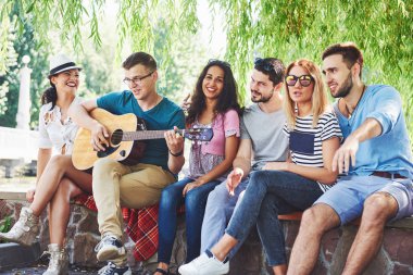 Gitarlı mutlu arkadaşlar grubu. Bir tanesi gitar çalarken diğerleri de onu alkışlıyor..