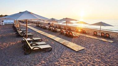 Kumsaldaki kumlu sahilin manzarası. Deniz ve dağlara karşı güneş yatakları ve şemsiyeler açık. Otelde. Tatil köyü. Tekirova-Kemer. Türkiye