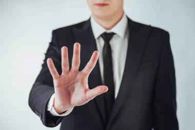 Takım elbiseli genç işadamı elini koyu bir arka planda gösteriyor.