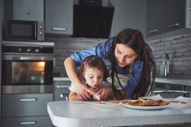 Mutfakta mutlu bir aile. Tatil yemeği konsepti. Anne ve kızı kurabiyeleri süsler. Ev yapımı hamur işleri yapan mutlu bir aile. Ev yapımı yemek ve küçük bir yardımcı..