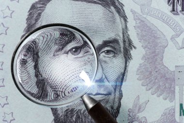 US President Abraham Lincoln face on the five dollar bill macro, 5 USD, US money close up under magnifying glass clipart
