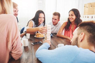 Bir grup yaratıcı arkadaş ahşap masada oturuyor. İnsanlar masa oyunu oynarken eğleniyor.
