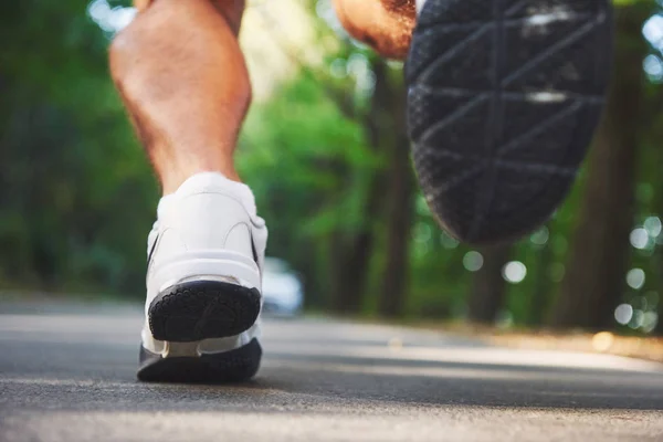 Outdoor cross-country running in concept for exercising, fitness and healthy lifestyle. Close up of feet of young runner man running along road in the park.