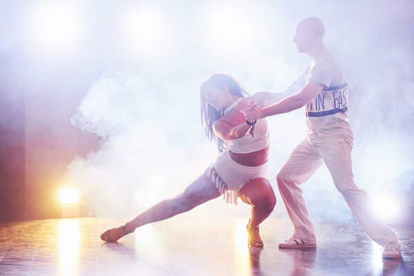 Skillful dancers performing in the dark room under the concert light and smoke. Sensual couple performing an artistic and emotional contemporary dance.