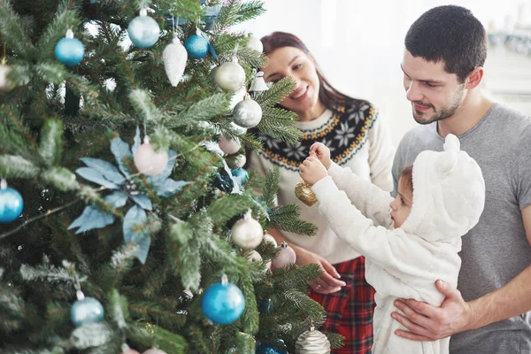Happy Family Decorating Christmas Tree together. Father, Mother And Daughter. Cute Child