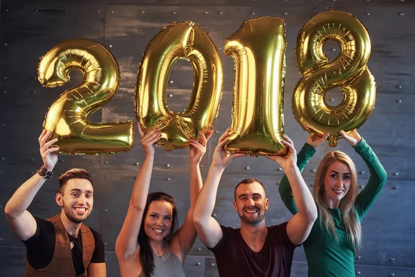 A group of merry young people hold numbers indicating the arrival of a new 2018 year. The party is dedicated to the celebration of the new year. Concepts about youth togetherness lifestyle.
