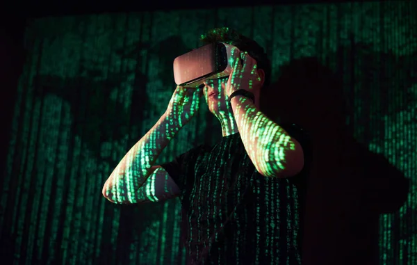 Double exposure of a caucasian man and Virtual reality VR headset is presumably a gamer or a hacker cracking the code into a secure network or server, with lines of code in green