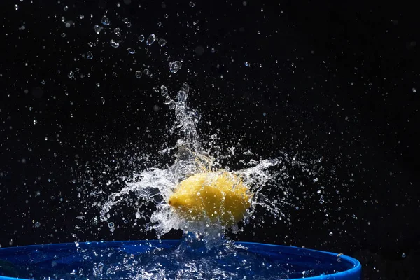 黒を背景に青い水に落ちる黄色のレモン — ストック写真