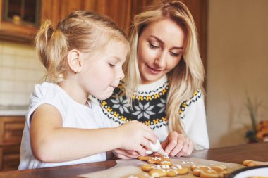 Anne ve kızı Noel kurabiyelerini beyaz şekerle süslüyor..