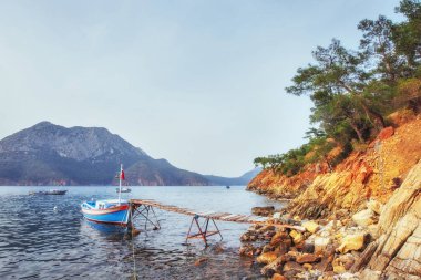 Kırık rıhtımın yakınındaki tekneler sakin, mavi bir deniz suyu koyuyor..