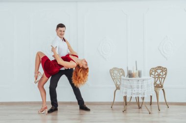 Kırmızı elbiseli genç bir kadın ve dans eden bir adam, stüdyoda beyaz bir arka planda izole edilmiş.