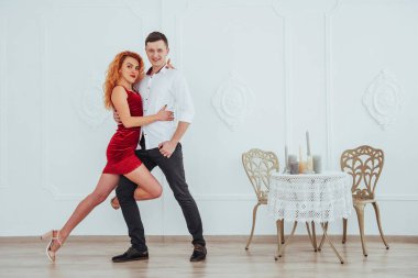 Kırmızı elbiseli genç bir kadın ve dans eden bir adam, stüdyoda beyaz bir arka planda izole edilmiş.