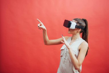 Mutlu gülümseyen güzel bir kızın portresi, kırmızı arka planda izole edilmiş sanal gerçeklik gözlüklerini kullanarak deneyim kazanmak.