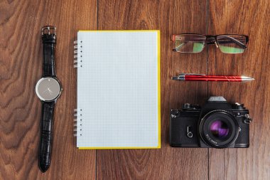 Kahverengi arkaplanda saat, kamera ve defter.