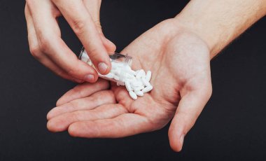 Bir adamın elinde cam kavanoz olan beyaz tabletler..