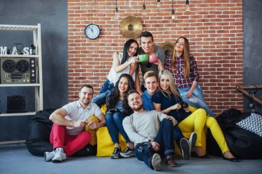 Çok ırklı erkek ve kızların renkli elbiseli arkadaşlarının toplu portresi ve bir tuğla duvarda poz vermeleri, insanların eğlenmesi, gençlik ve birliktelik konseptleri..