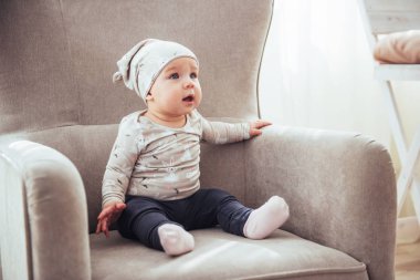 1 year girl wearing stylish clothes, sitting in a vintage chair in the room. Childhood.