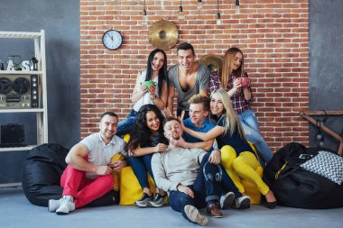 Çok ırklı erkek ve kızların renkli elbiseli arkadaşlarının toplu portresi ve bir tuğla duvarda poz vermeleri, insanların eğlenmesi, gençlik ve birliktelik konseptleri..