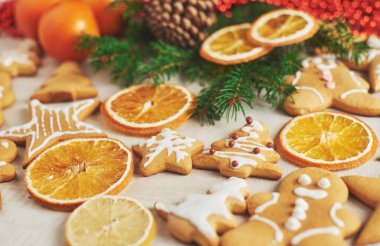 Noel kurabiyeleri, kurutulmuş portakal ve baharatlar beyaz masada. Sandalyeler, Noel ağaçları, koniler ve Noel süslemeleri.