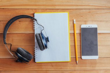 Kulaklıklar, defter ve kalem kahverengi ahşap arka planda..