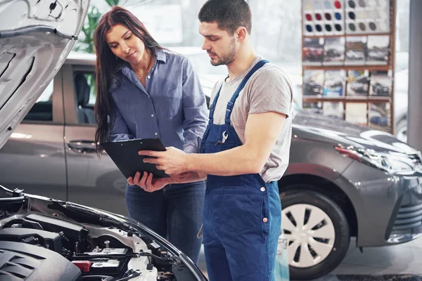 A man mechanic and woman customer discussing repairs done to her vehicle.