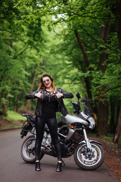 一个穿着皮衣 性感迷人的女孩站在外面的一辆摩托车旁边 — 图库照片