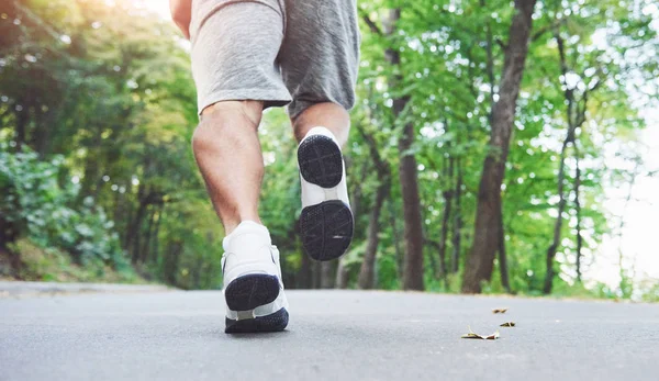 Outdoor cross-country running in concept for exercising, fitness and healthy lifestyle. Close up of feet of young runner man running along road in the park.