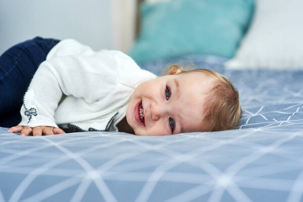 Friendly baby girl smile lying on the bed.